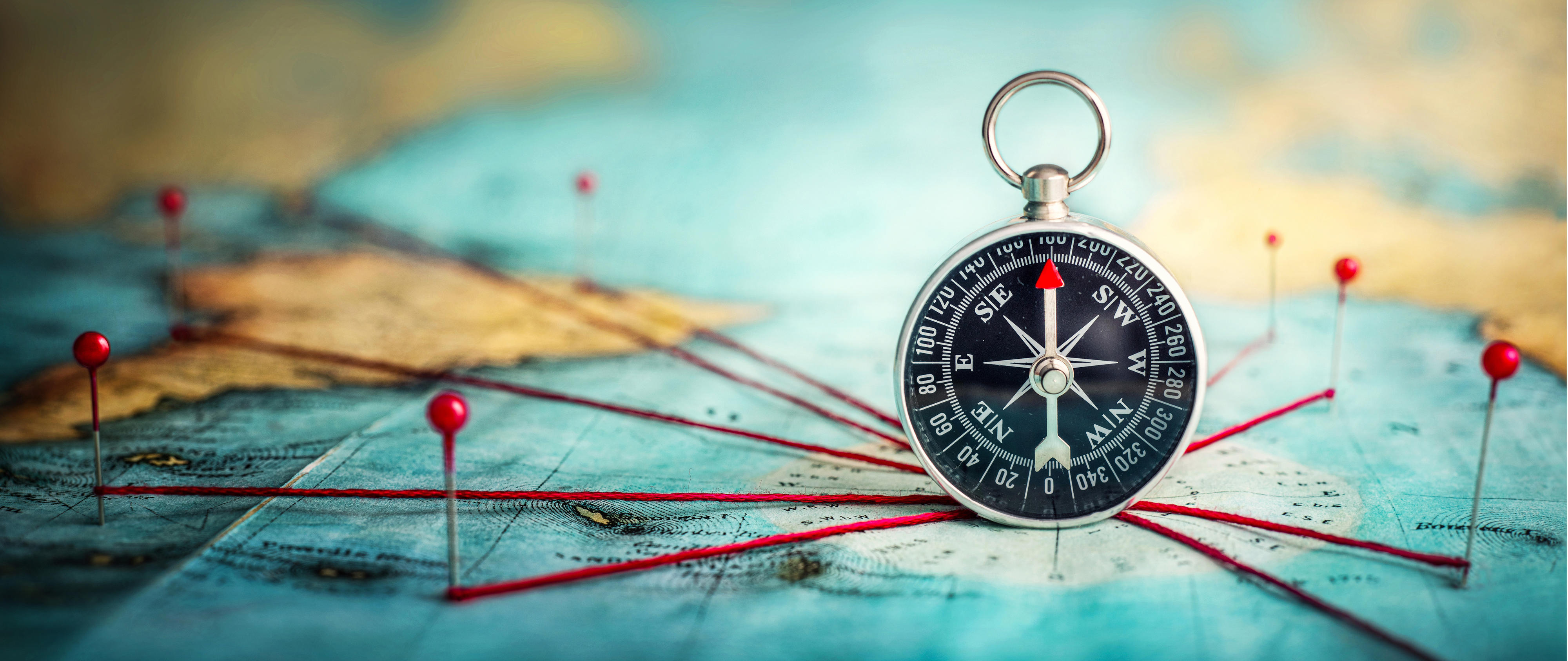 Magnetic compass and location marking with a pin on routes on world map. Adventure, discovery, navigation, communication, logistics, geography, transport and travel theme concept background.. Macro photo. Very shallow focus.